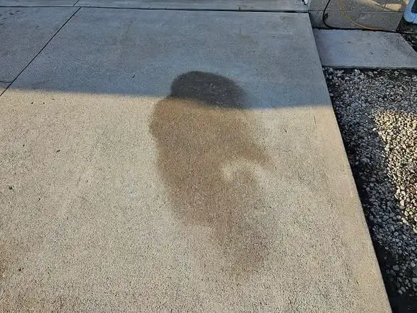 Dark oil stain spreading across a concrete driveway surface