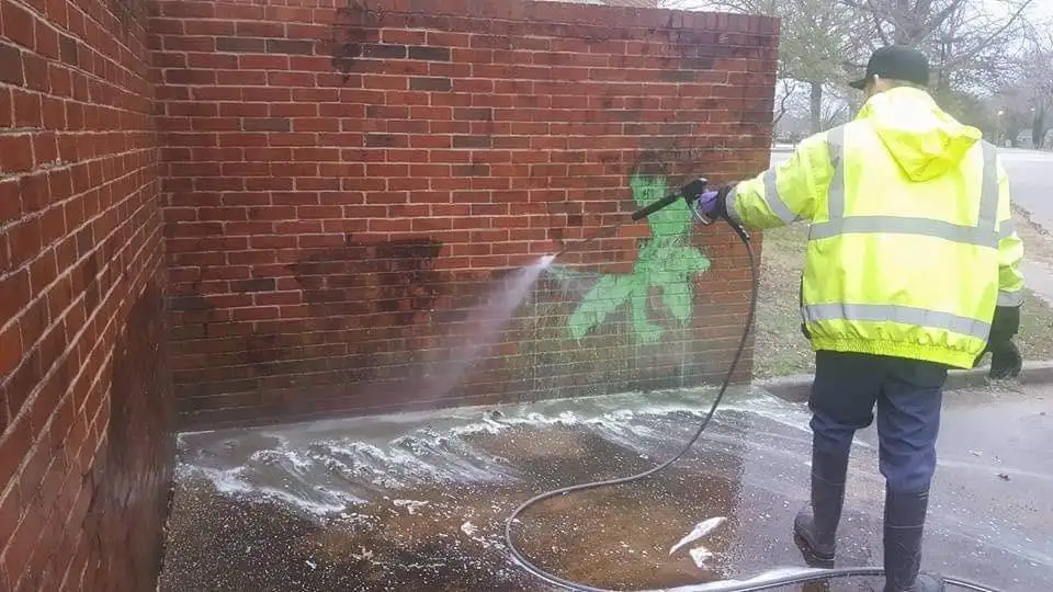 Dallas graffiti removal technician rinsing spray paint off a brick wall