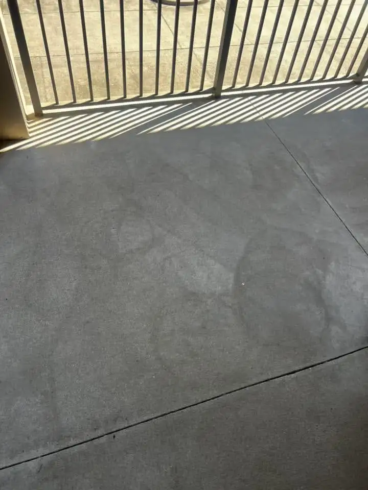 Uneven dark streaks and patches on a concrete patio floor beside a metal railing