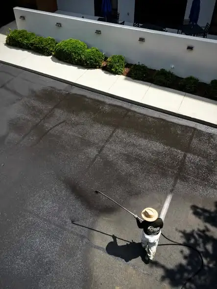 Worker pressure washing a parking lot beside a landscaped storefront wall